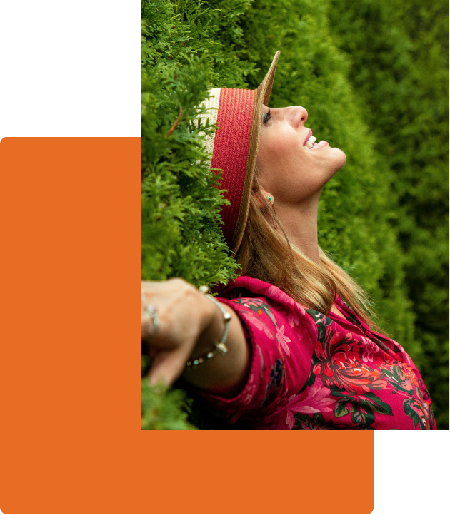 woman in a hat with arms outstretched in foliage happy and smiling